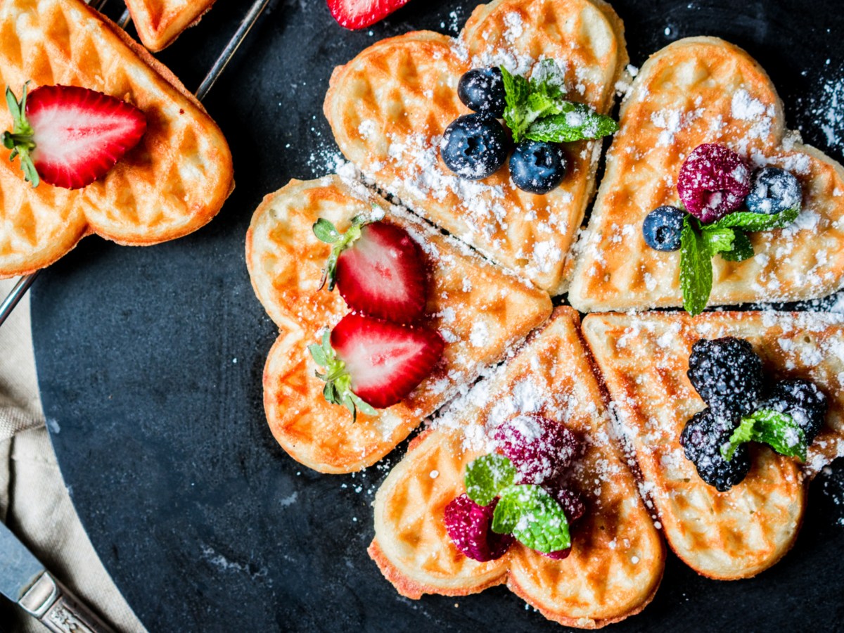 Herzwaffeln mit Früchten auf dunklem Teller.