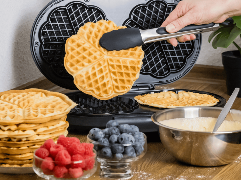 Person backt Herzwaffeln in Waffeleisen.
