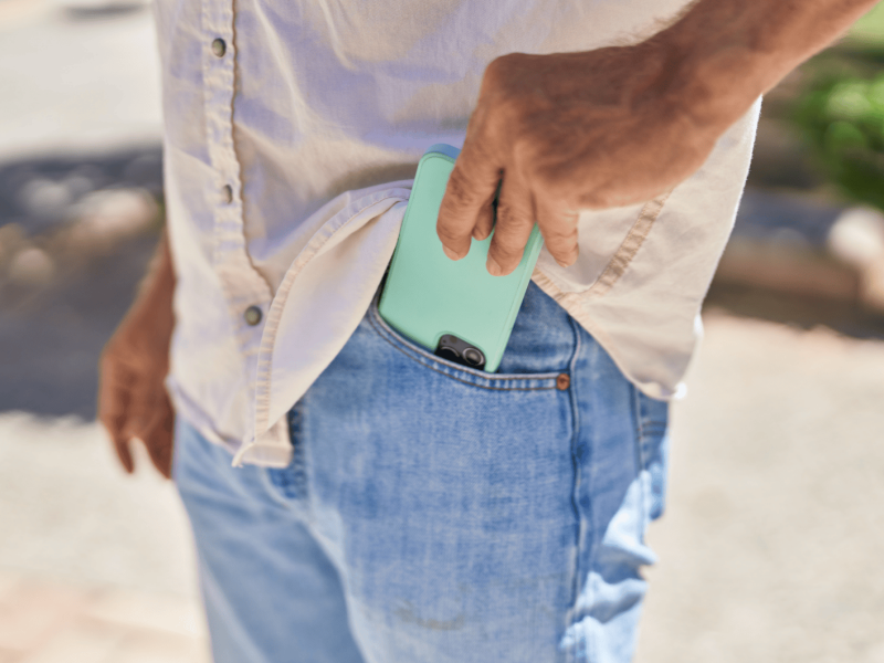 Mann steckt Handy in seine vordere Hosentasche.