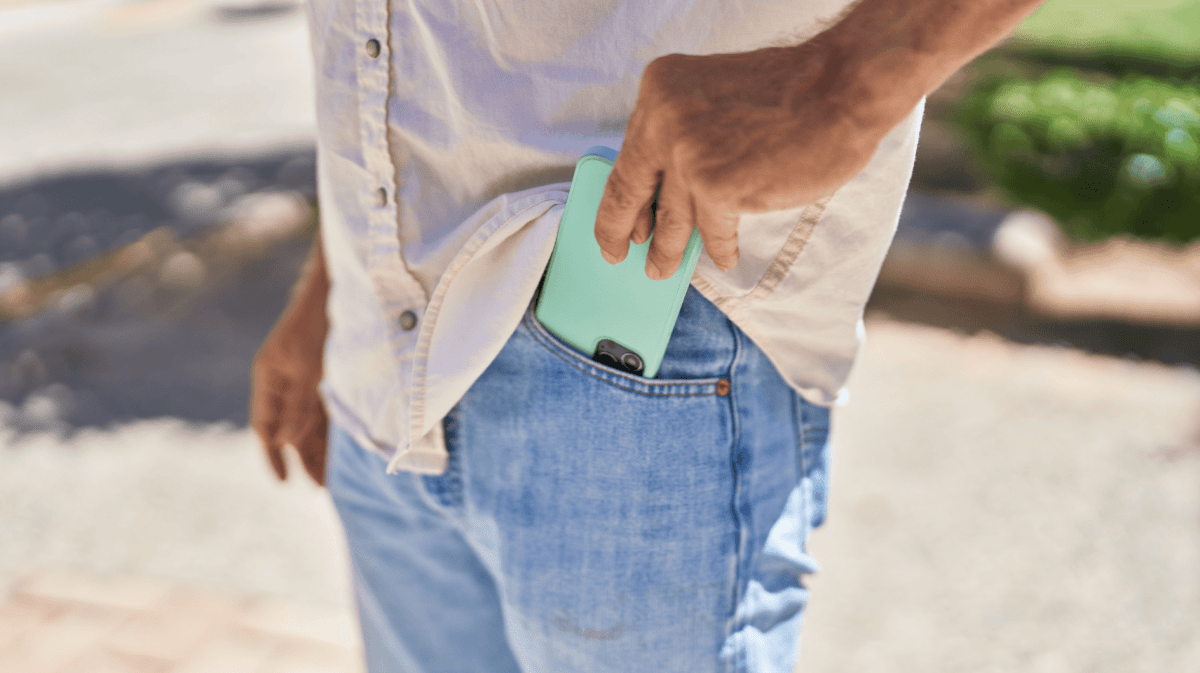 Mann steckt Handy in seine vordere Hosentasche.