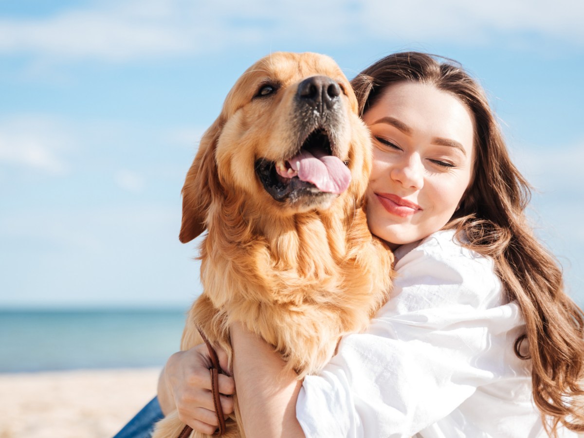 Frau kuschelt Hund am Strand.