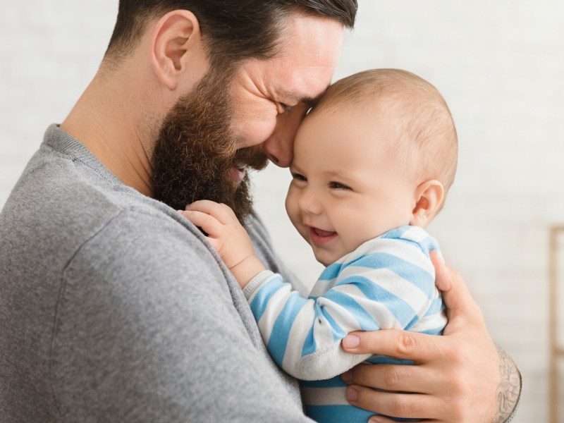 Vater hält sein Baby auf Arm und lächelt.