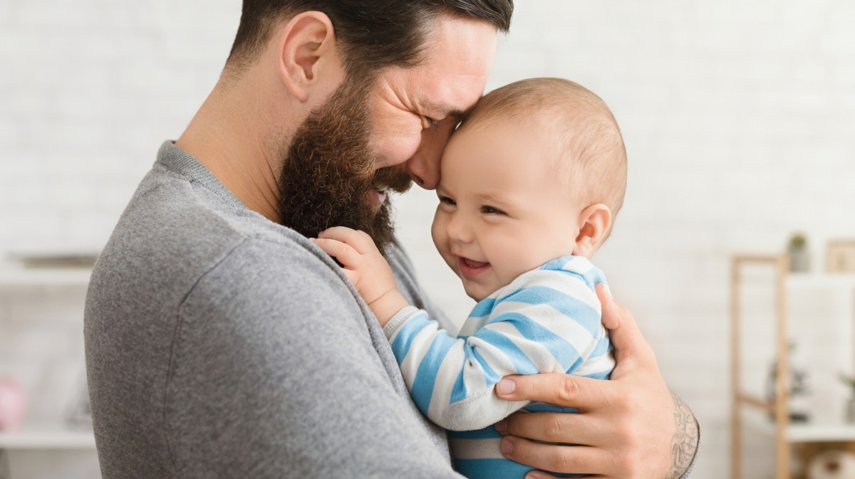 Vater hält sein Baby auf Arm und lächelt.