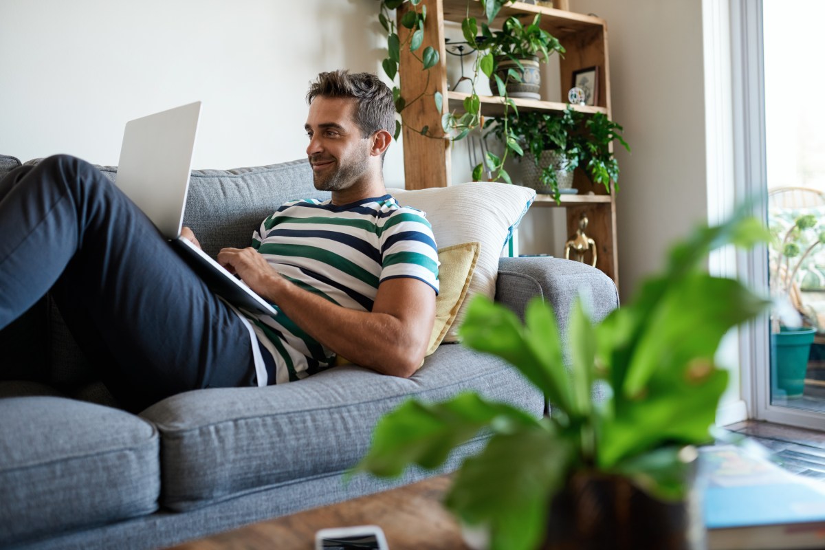 Mann sitzt zufrieden lächeln mit Laptop auf der Couch