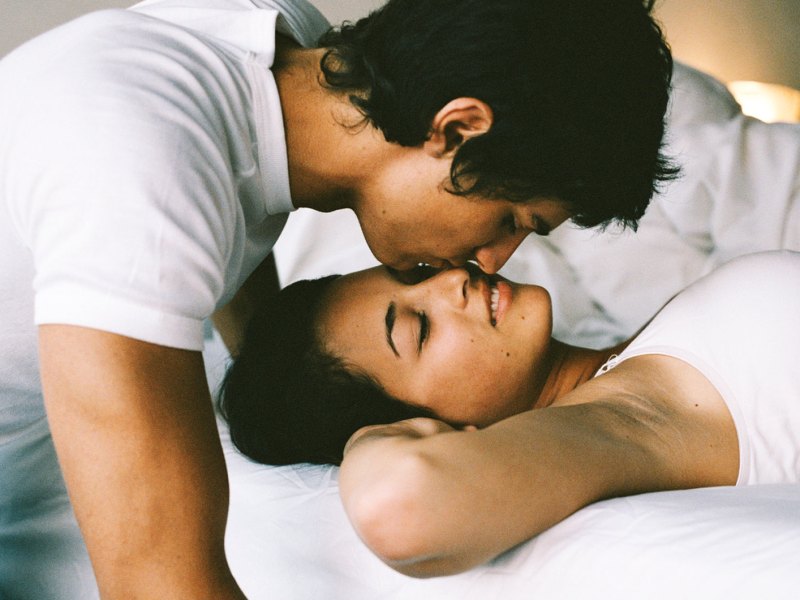 Mann küsst Frau auf die Stirn, während beide im Bett liegen.