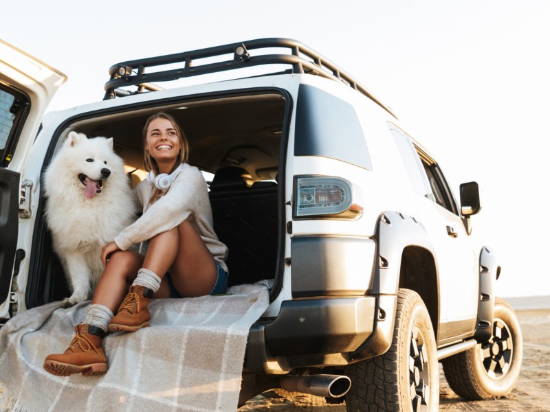 Frau mit Hund im Kofferraum eines Geländewagens
