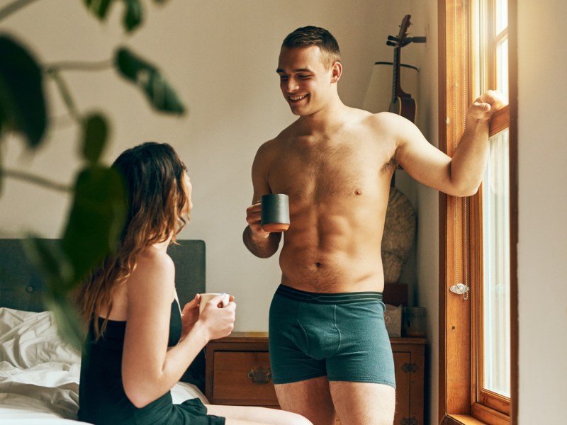 Frau und Mann in Unterwäsche vor Bett mit Kaffee in der Hand