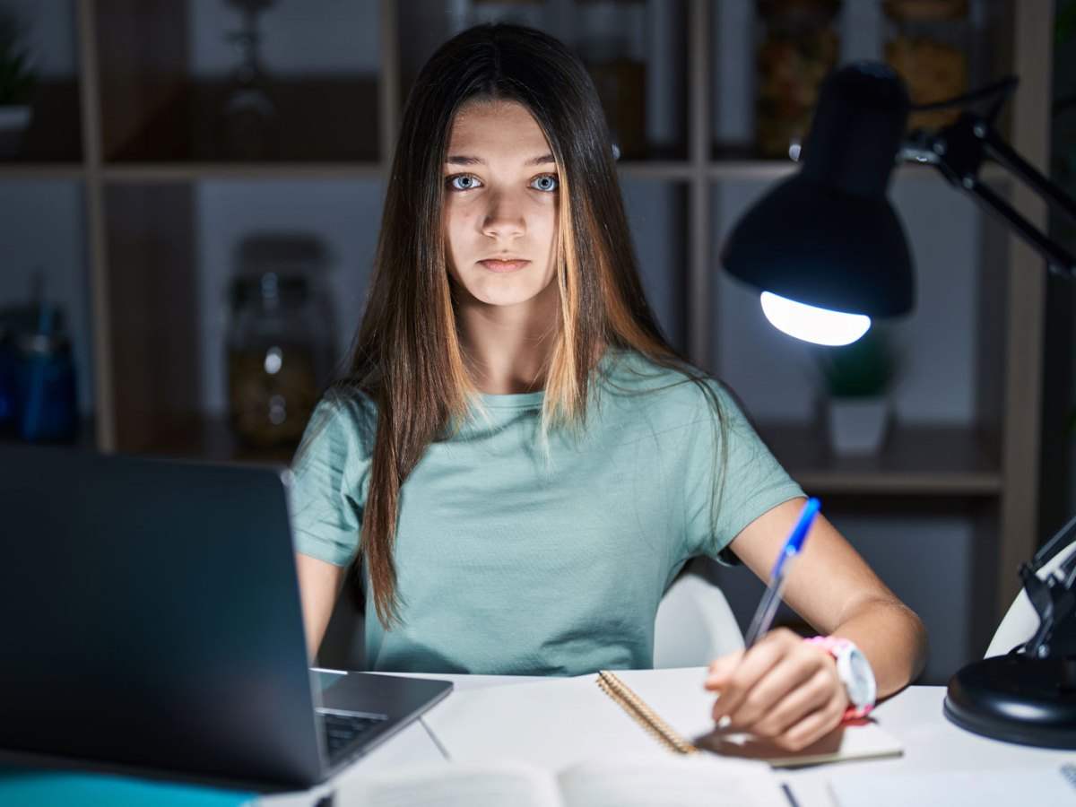 Teenagerm&auml;dchen sitzt im Dunkeln an ihrem Schreibtisch, der von einer Schreibtischlampe beleuchtet wird und lernt.