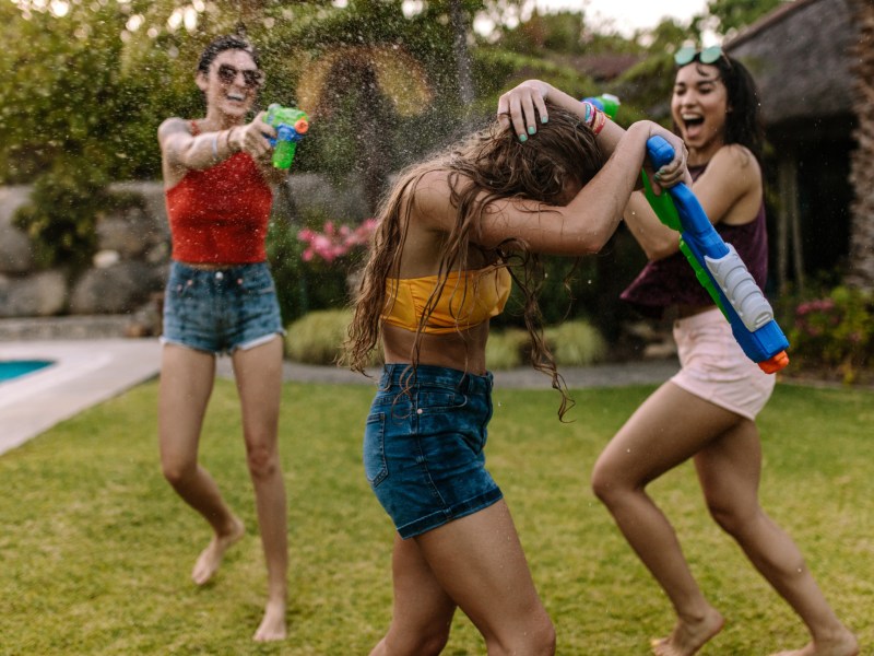 Drei Freundinnen machen eine Wasserschlacht im Garten