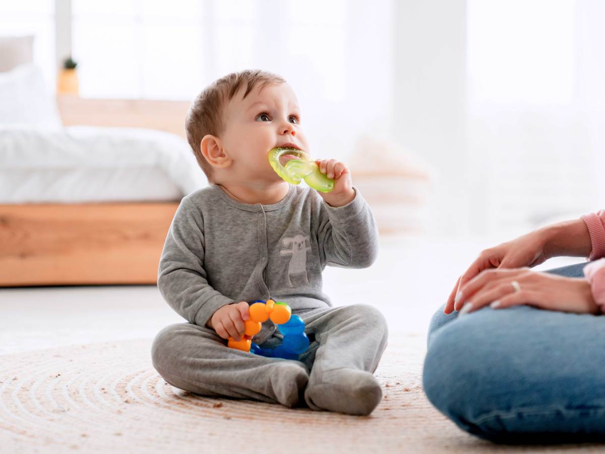 Baby sitzt auf dem Boden und kaut auf einem Beißring herum.