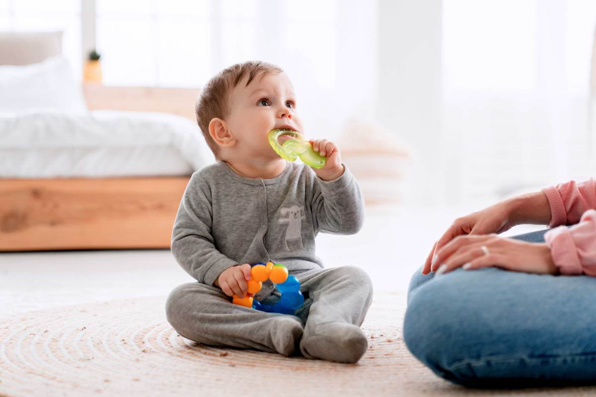 Baby sitzt auf dem Boden und kaut auf einem Beißring herum.