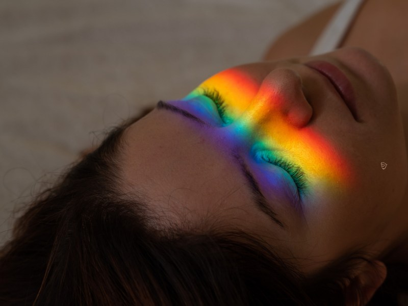 Frau, die auf dem Boden liegt und einen Regenbogen im Gesicht hat.