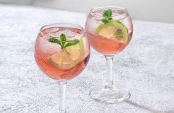 Sarti Spritz: Hellrosa Getränk in Weingläsern mit Limettenscheiben