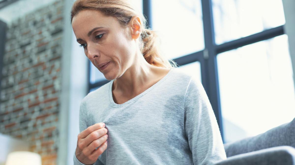 Frau schwitzt in ihrem Shirt stark und versucht es auszulüften.