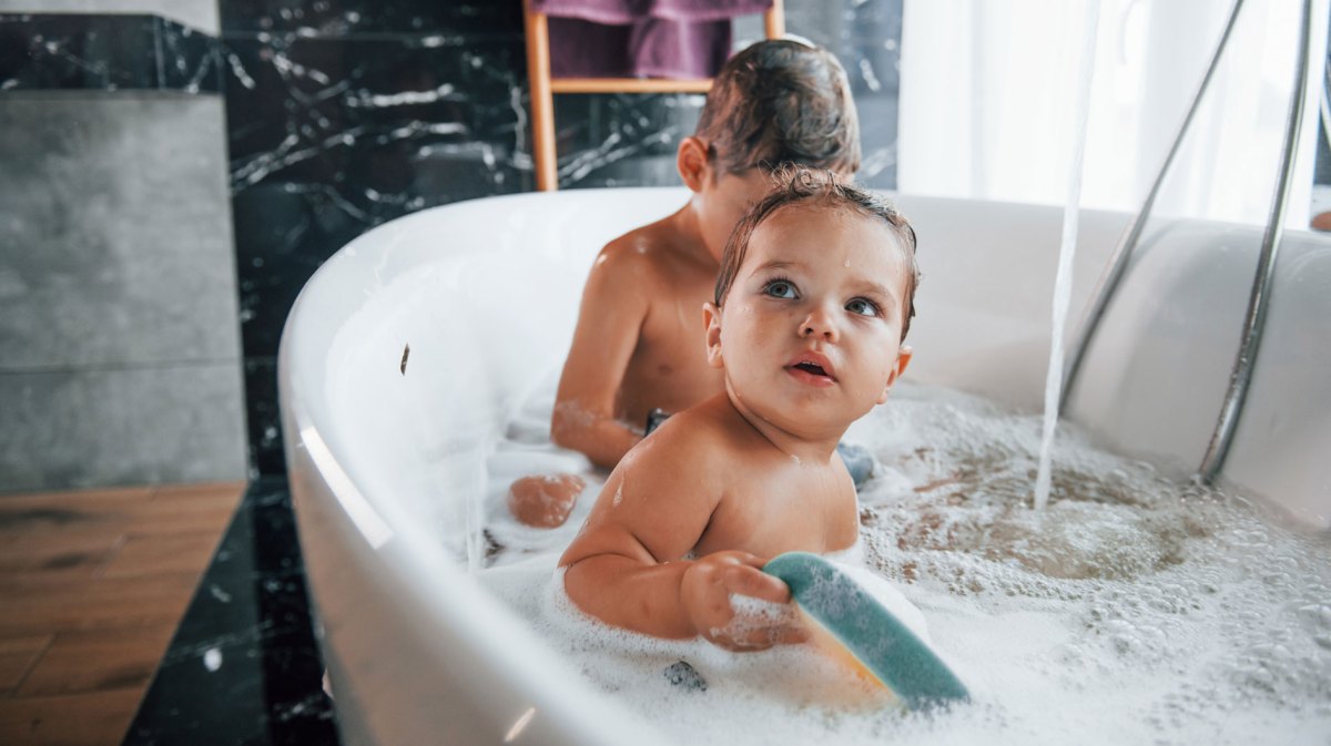 Geschwister sitzen in der Badewanne mit Schaum und Spielzeug.