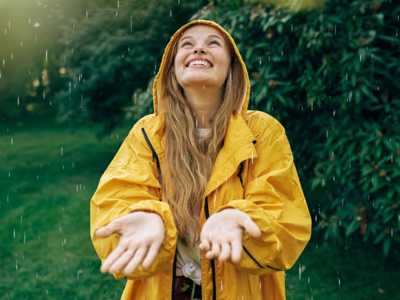 Frau genießt den Regen, während die Sonne scheint.