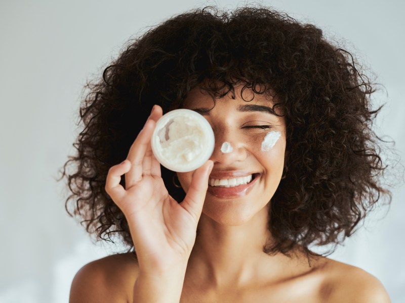 Antifaltencreme-test: Frau trägt Creme auf Gesicht auf und lacht