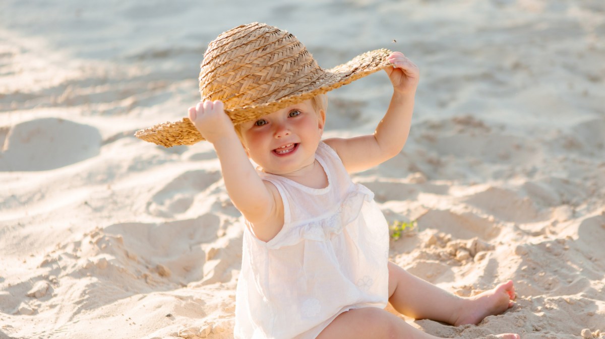 Baby am Strand mit Sonnenhut auf dem Kopf, das in die Kamera lächelt