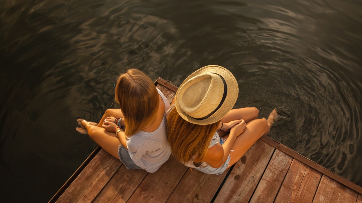 Zwei Frauen am Ufer auf Steg, die in die entgegengesetzte Richtung schauen und sitzen