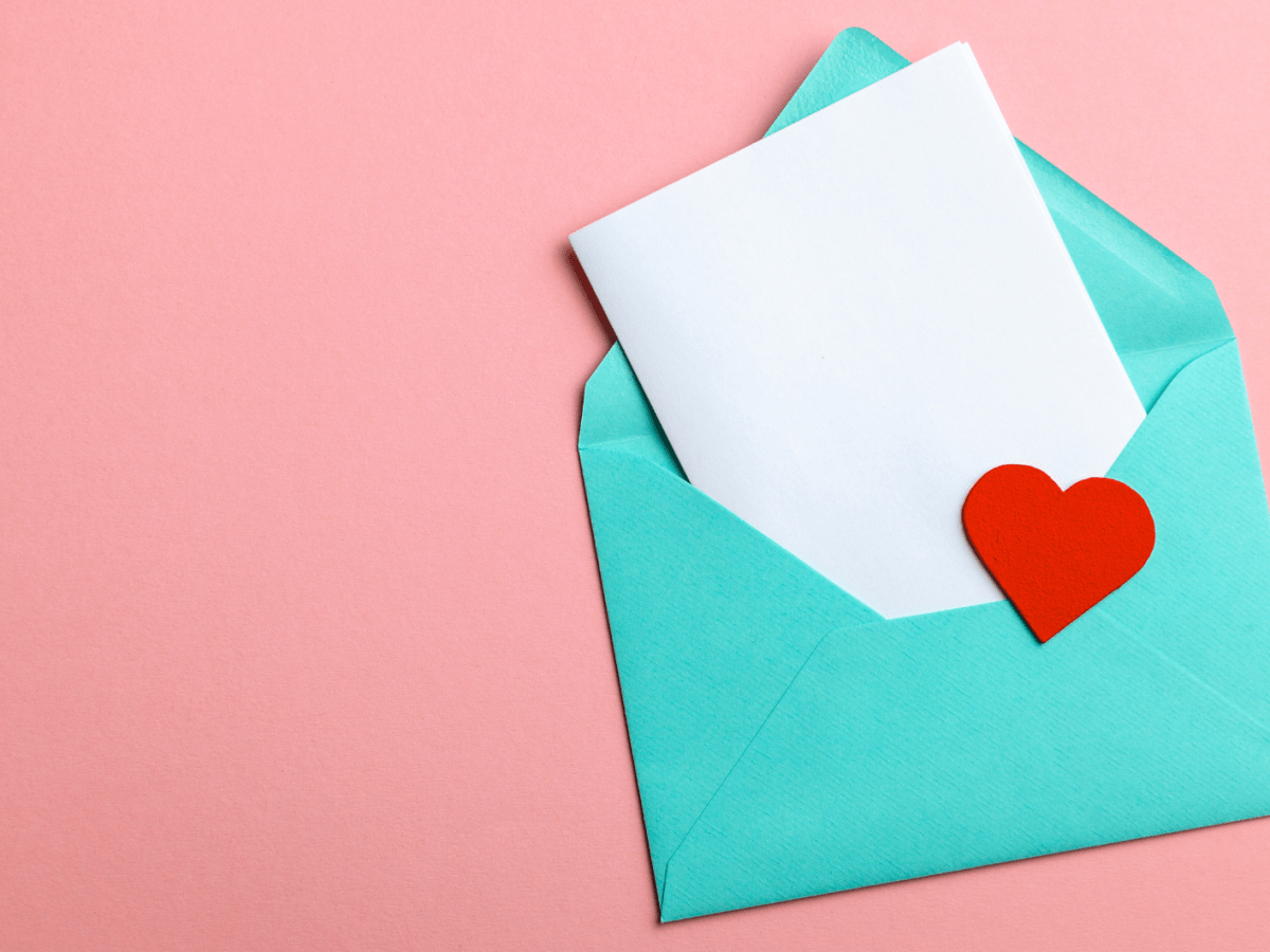 Ge&ouml;ffneter t&uuml;rkisfarbener Umschlag mit wei&szlig;em Papier und einem roten Herz auf zartem rosafarbenem Untergrund.