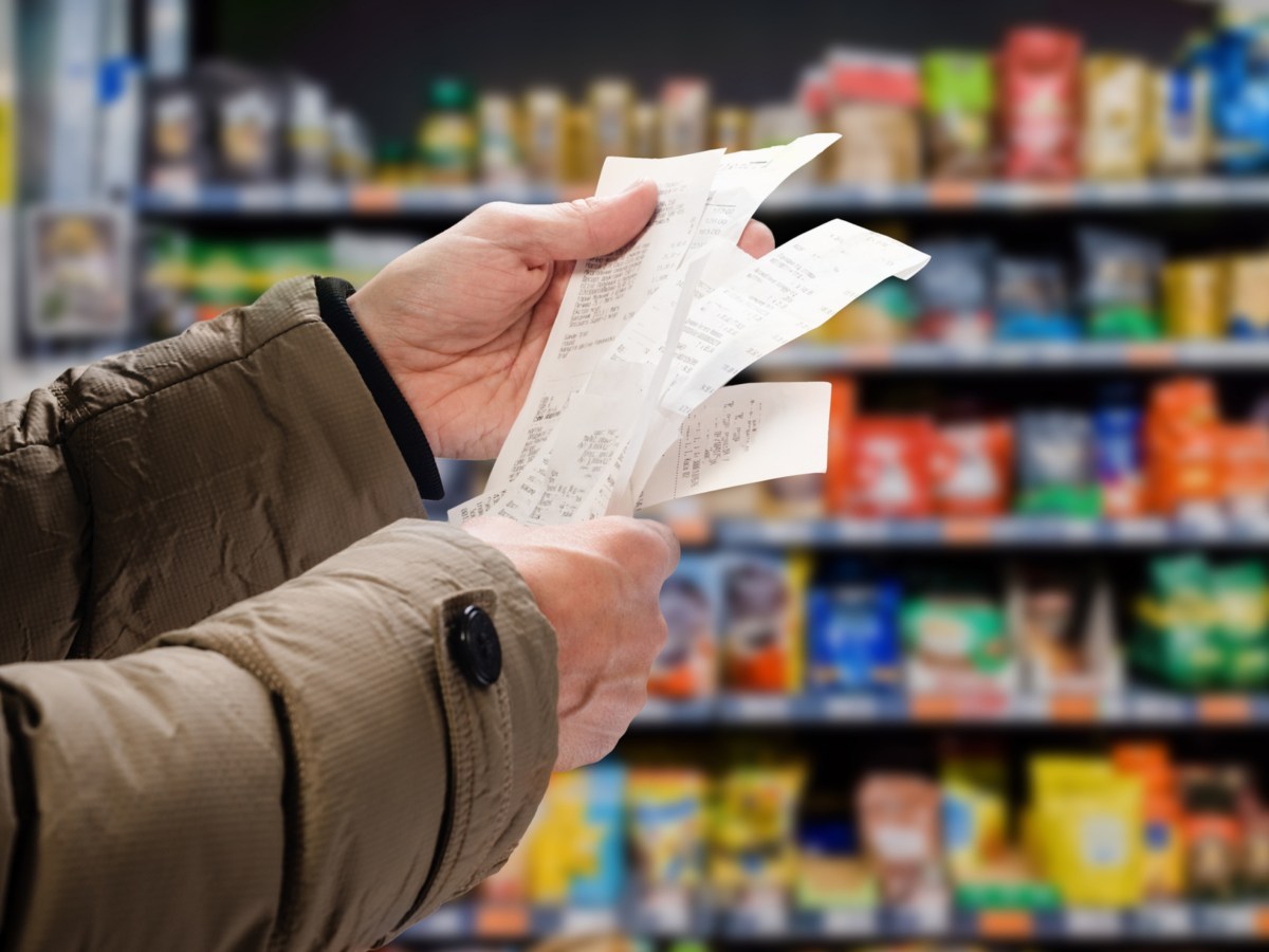 Arme eines Mannes, der im Supermarkt drei Kassenzettel liest und vergleicht