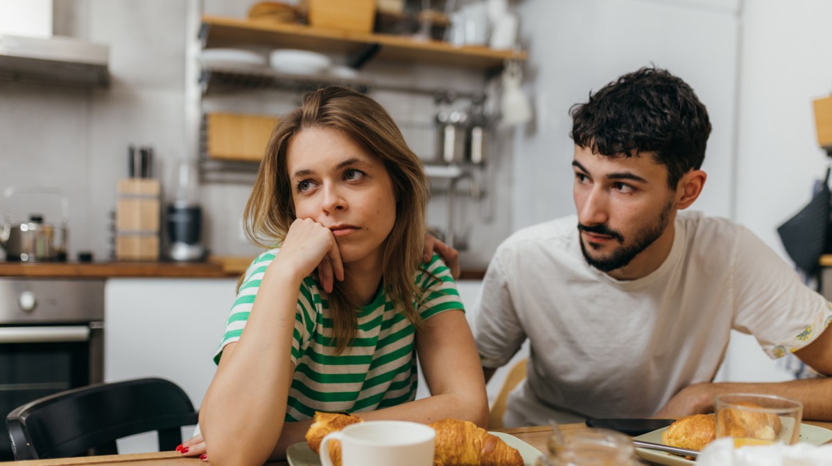 Frau und Mann in Küche beim Frühstück, die genervt zur Seite schauen
