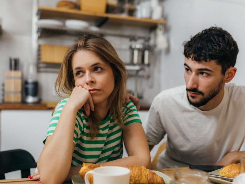 Frau und Mann in Küche beim Frühstück, die genervt zur Seite schauen