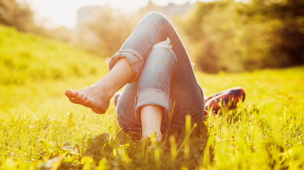 Person in Jeans liegt auf einem sonnigen Rasen.
