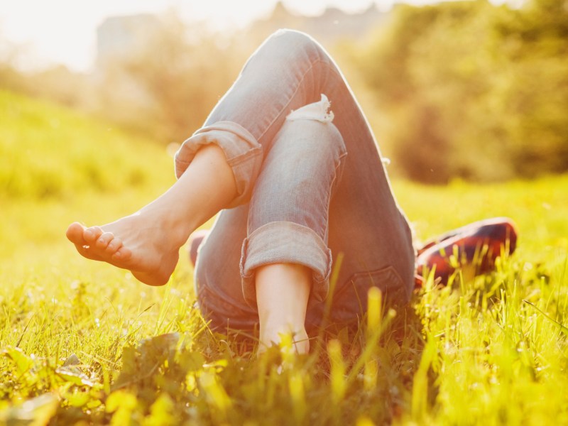 Person in Jeans liegt auf einem sonnigen Rasen.