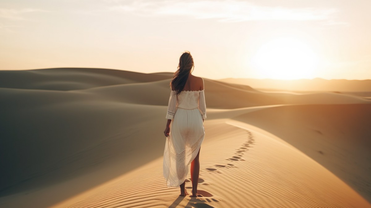 Frau in Wüste beim Sonnenuntergang in weißem Kleid