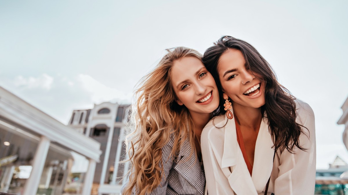 Zwei Frauen lachend vor Kamera mit Stadt im Hintergrund