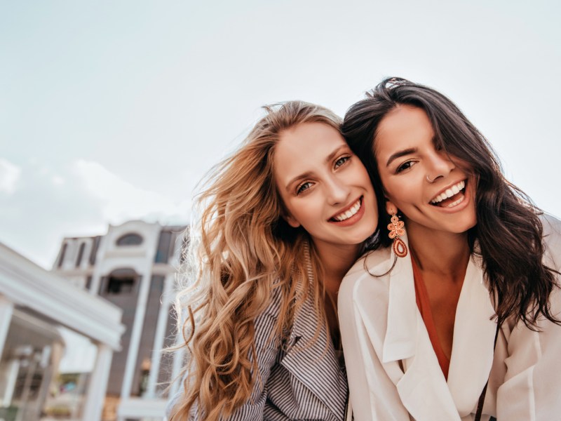 Zwei Frauen lachend vor Kamera mit Stadt im Hintergrund