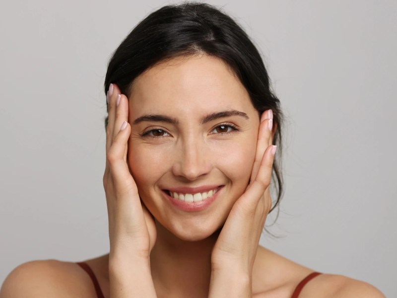 Schöne Frau mit reiner Haut hält sich das Gesicht fest