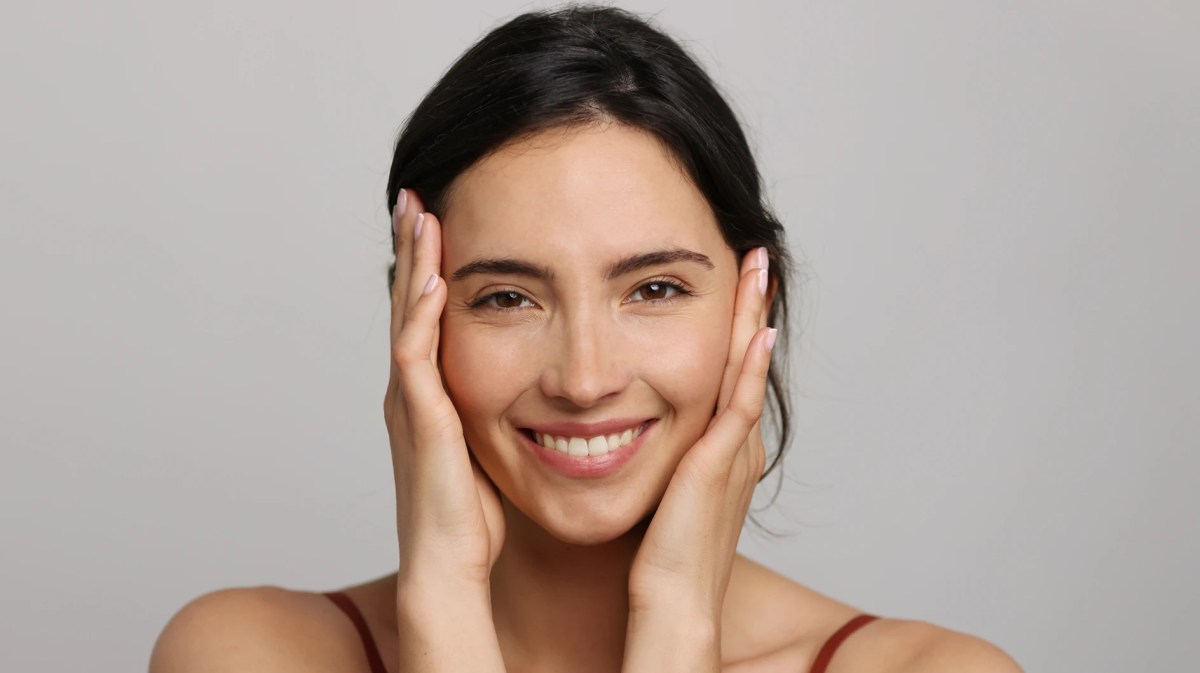 Schöne Frau mit reiner Haut hält sich das Gesicht fest