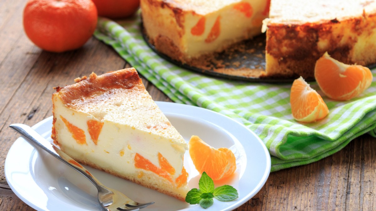 Käsekuchen mit Mandarinen auf weißem Teller.