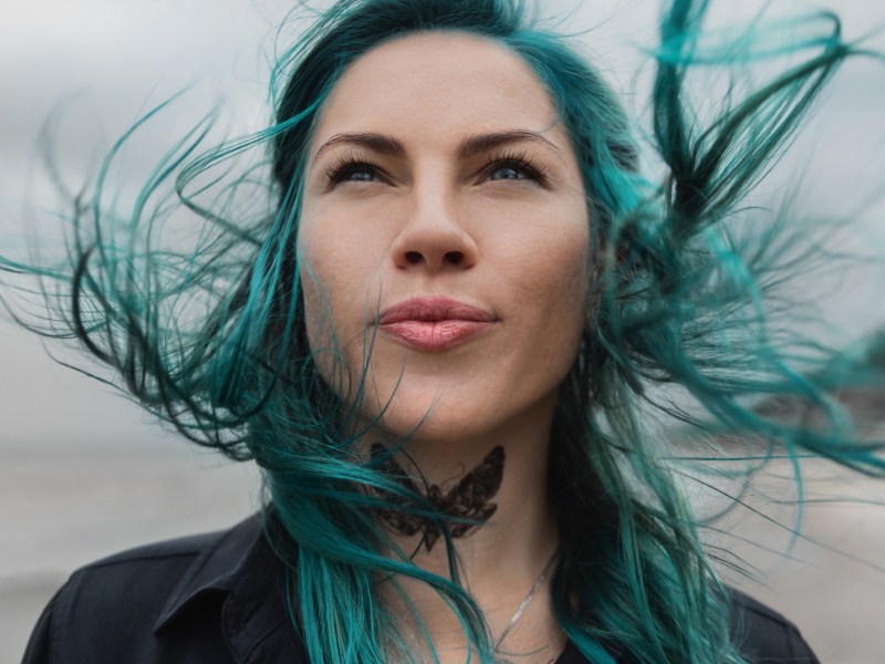 Frau mit blauen Haaren steht am Strand.