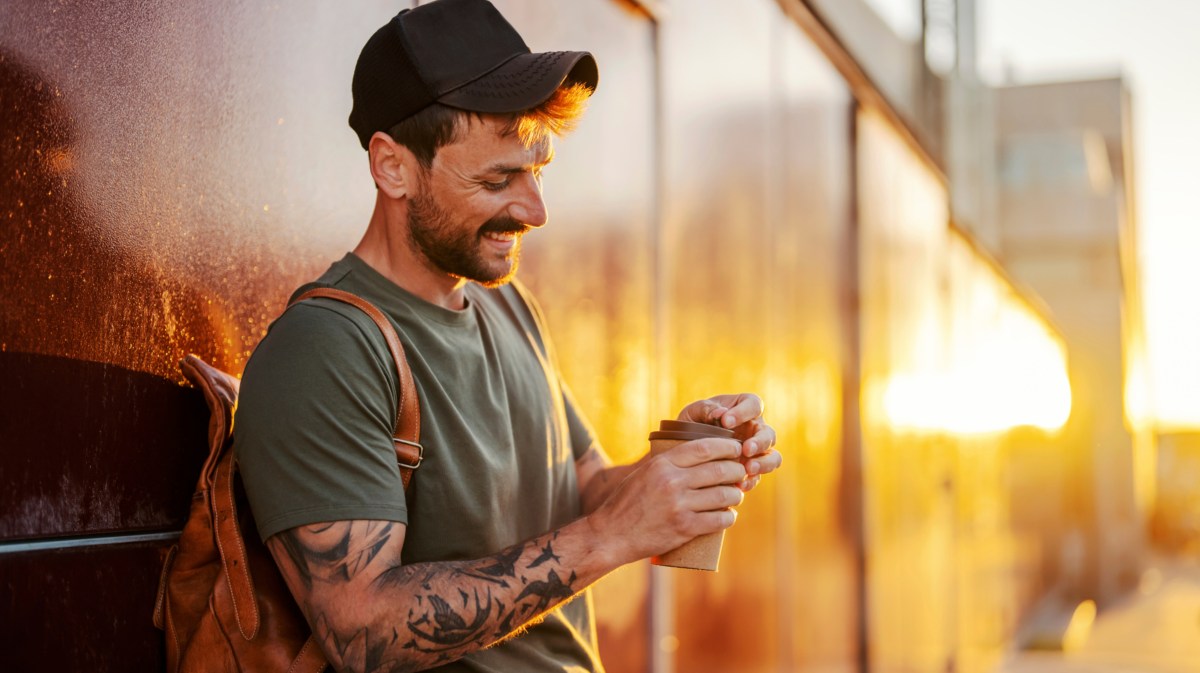 Mann mit Tattoos trinkt To-Go-Kaffee.