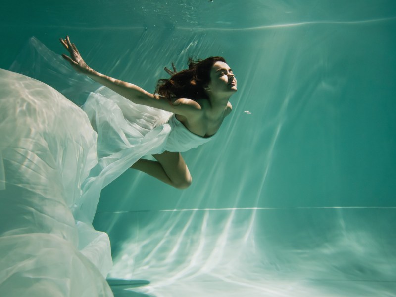 Frau schwimmt in weißem Kleid.