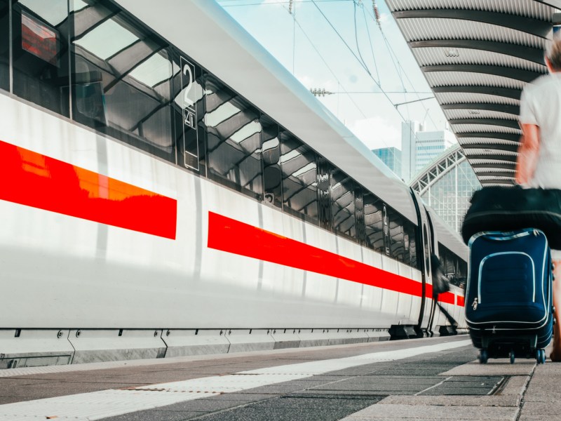 Zug der deutschen Bahn, der gerade einfährt, mit einem Mann am rechten Bildrand, der seinen Koffer hinter sich herzieht