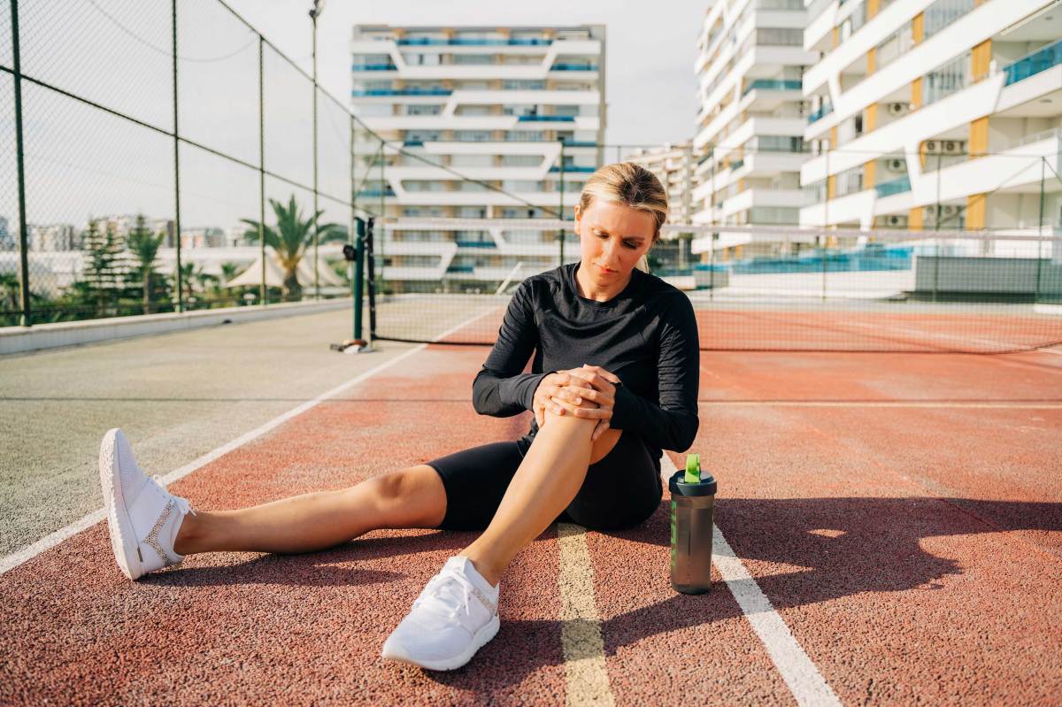 Athletische Frau hält sich das schmerzende Knie auf einem Tennisplatz