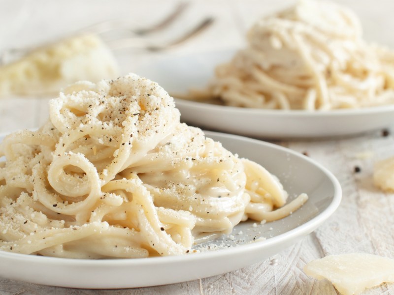 Spagetthi mit Käse und Parmesan serviert auf einem Tisch neben einem Stück Parmesan