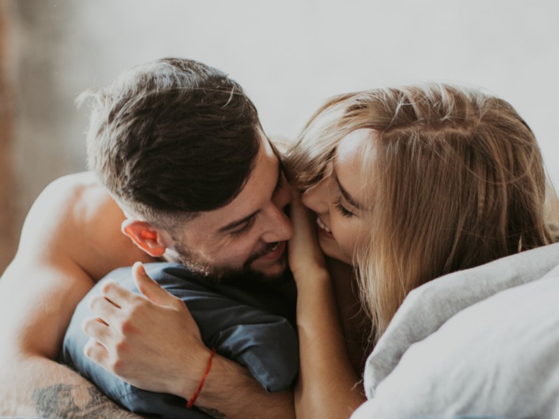 Frau und Mann im Bett zwischen Kissen, die sich anlächeln und umarmen