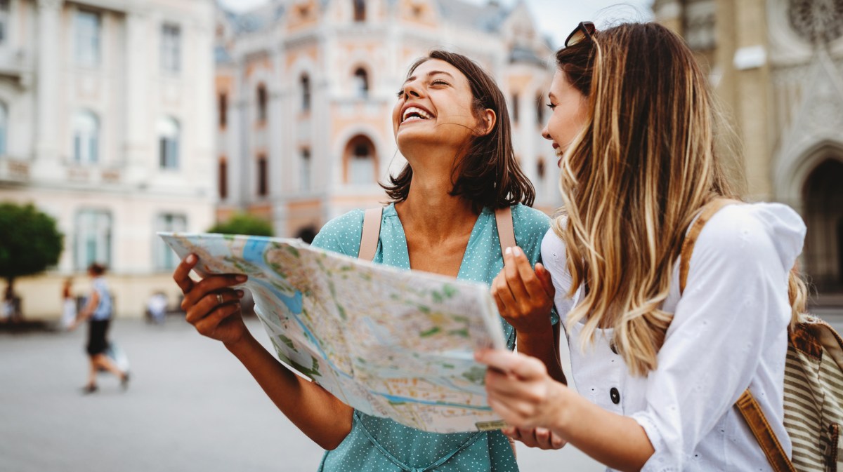 Zwei Frauen schauen gemeinsam auf eine Landkarte, lachen dabei