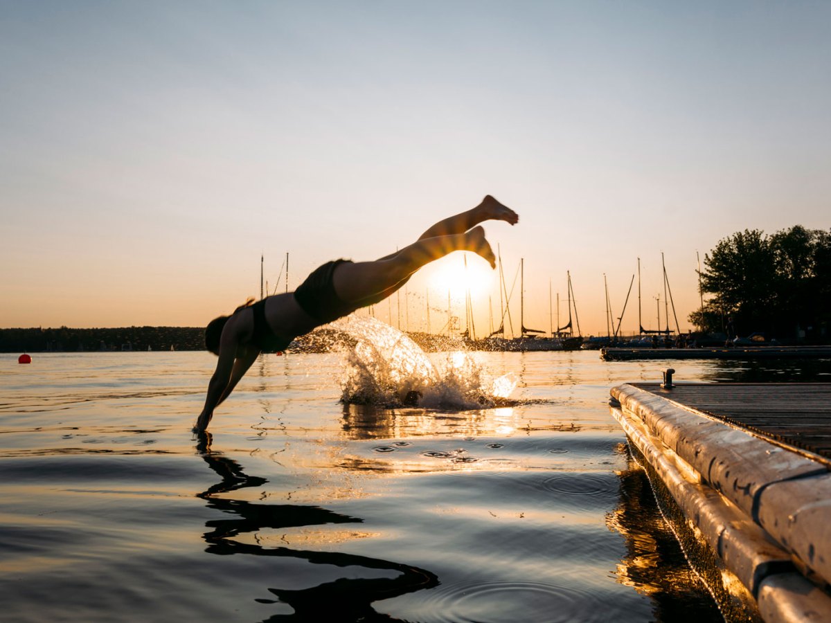Eine Frau macht bei Sonnenuntergang einen Kopfsprung in einen See.