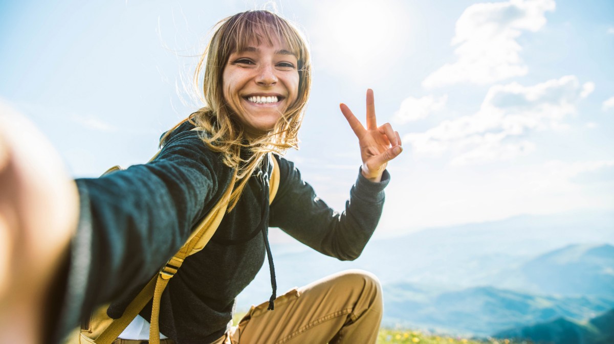 Frau sitzt auf Berg und lächelt in Kamera.