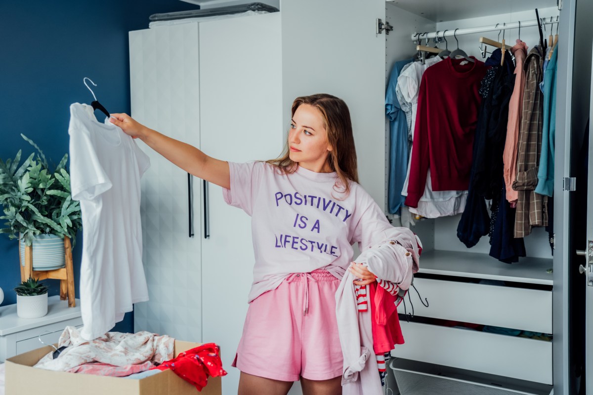 Junge Frau steht vor Kleiderschrank und schaut sich weißes T-Shirt an