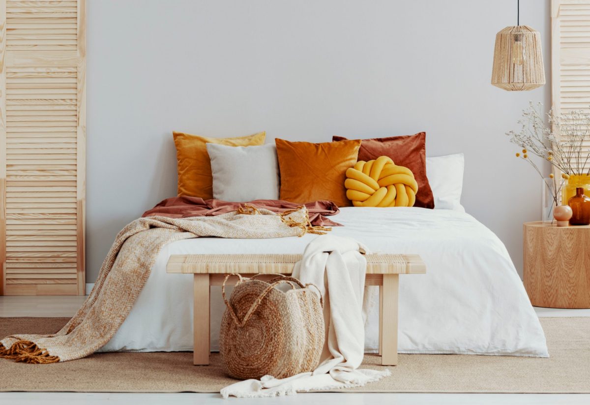 Bett dekoriert mit Kissen, einer Tagesdecke und einer Bank am Fußende