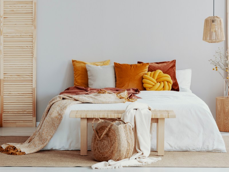 Bett dekoriert mit Kissen, einer Tagesdecke und einer Bank am Fußende