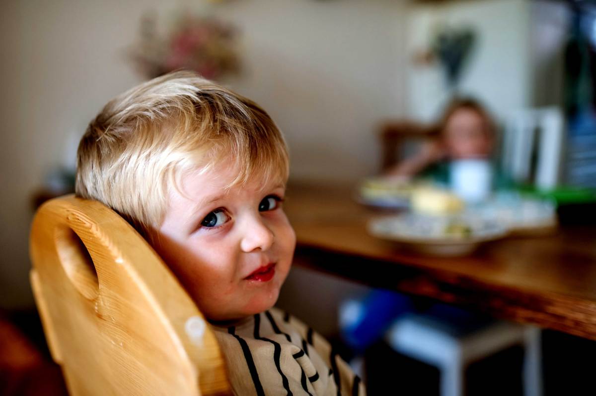 Kleiner Junge sitzt in seinem Hochstuhl am Küchentisch und schaut seitlich in die Kamera.