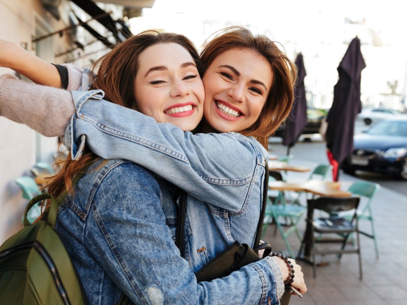 Zwei Frauen, die sich auf der Straße umarmen und in die Kamera lächeln
